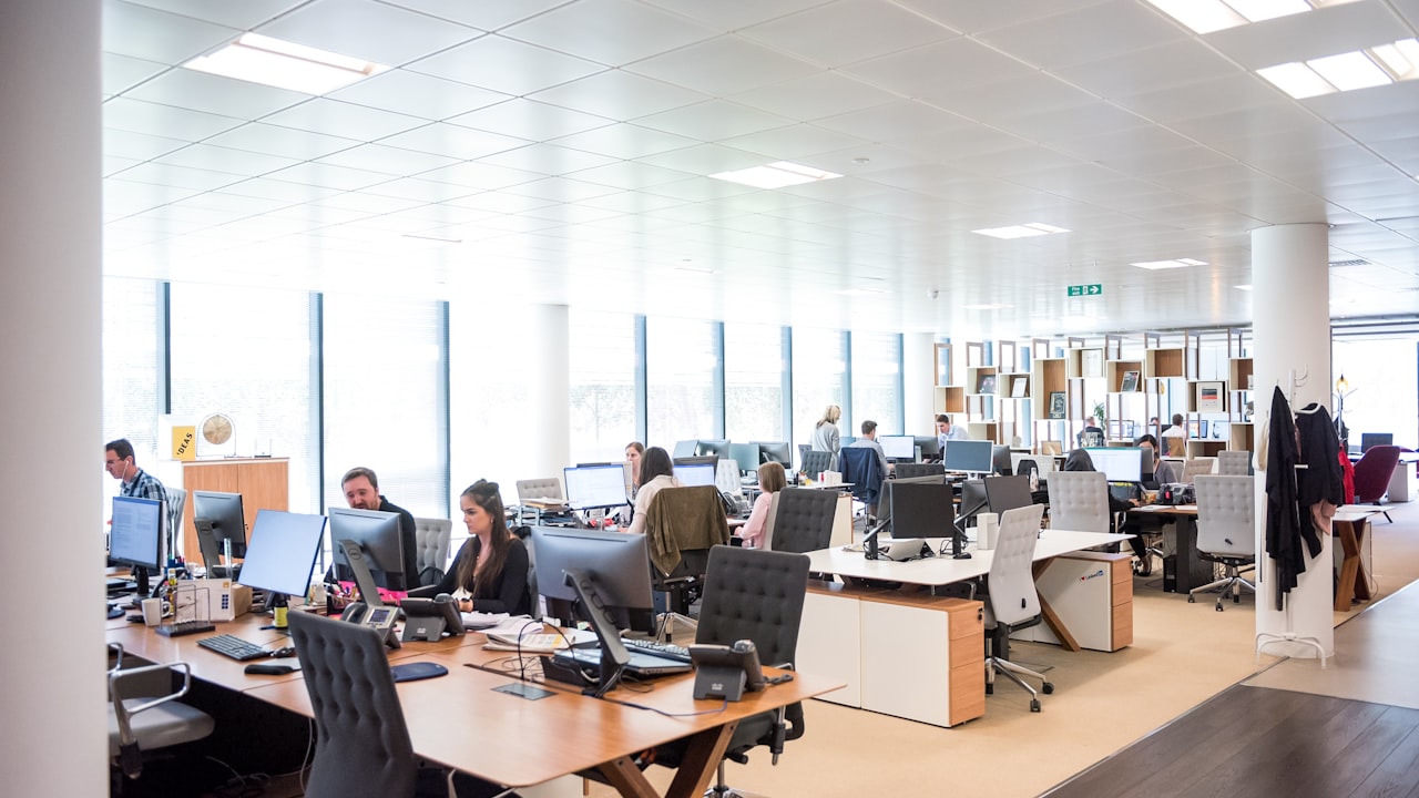 Open space d'entreprise avec plusieurs collaborateurs installés à leurs bureaux, chacun devant un ou plusieurs écrans d'ordinateur