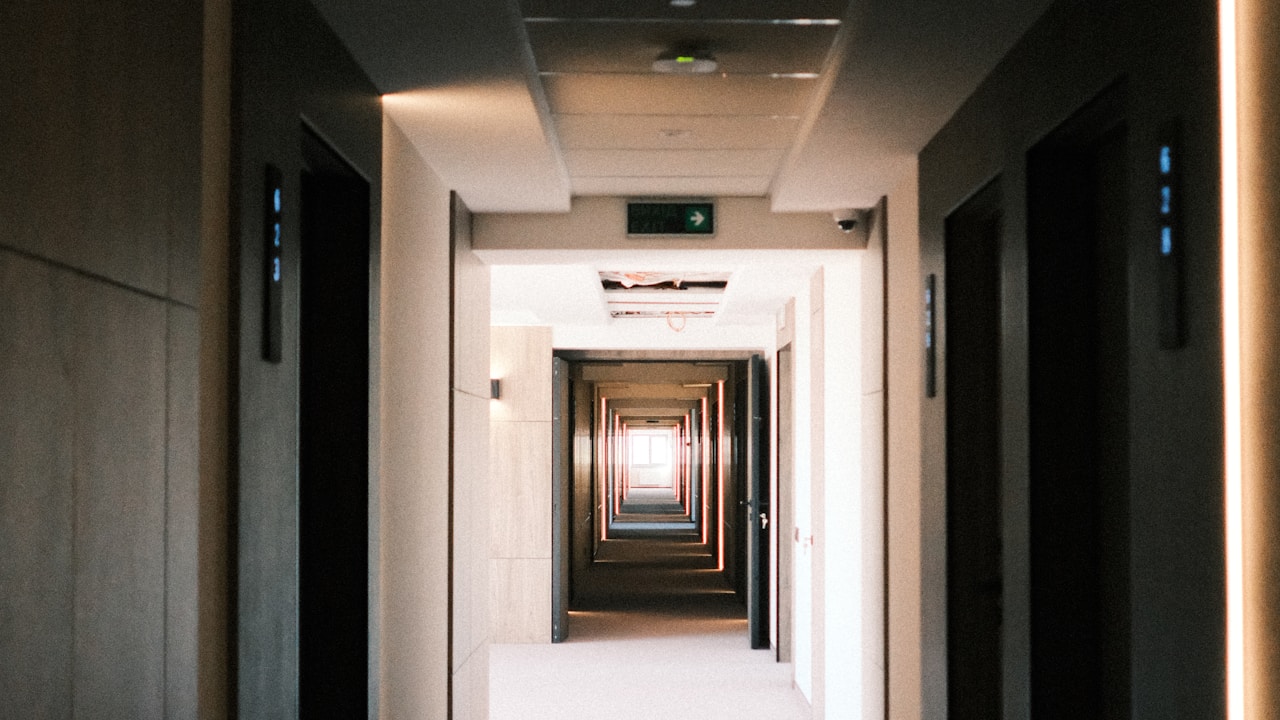 Couloir d'hôtel vide, faiblement éclairé, avec une perspective de portes de chambres qui se succèdent